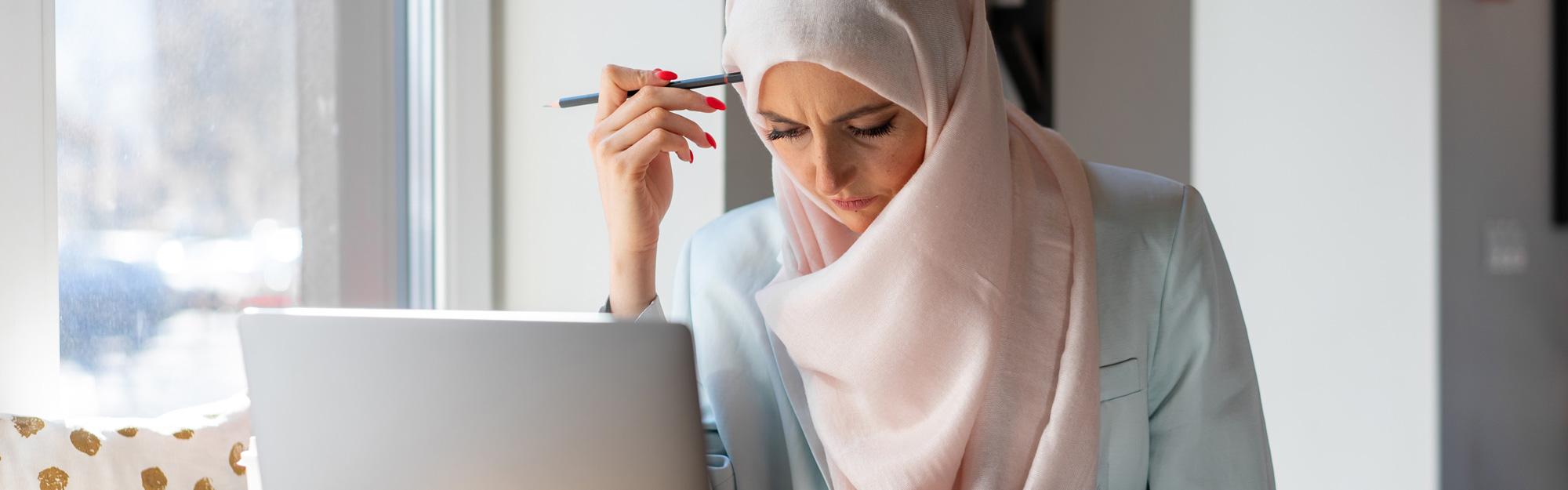 A Muslim woman sits at a laptop studying for her North Carolina content test.
