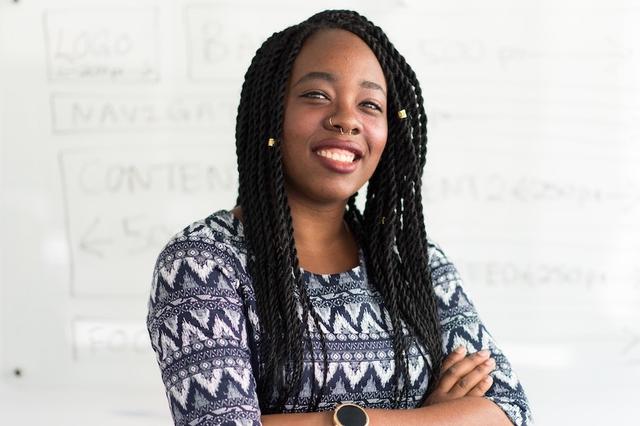 A smiling NC teacher stands in front of a classroom whiteboard